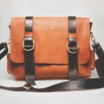 Elegant brown leather briefcase with dark straps and metal buckles, ideal for fashion and business.